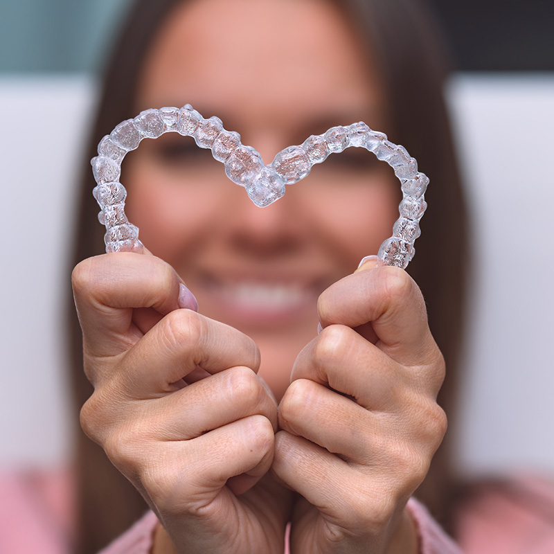 A smiling person holding up two hands with a heart-shaped plastic object in each hand.